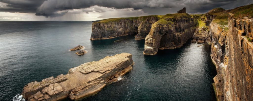 A dramatic view of Old Wicl Castle sitting on the cliffs on an overcast day