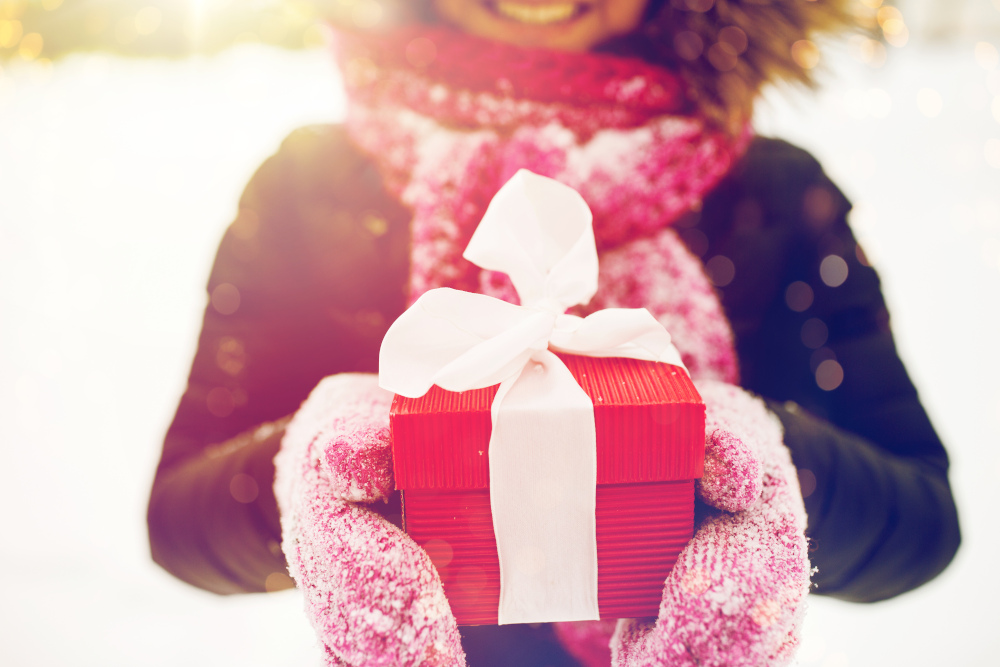 Woman in the snow, holding out a wrapped gift