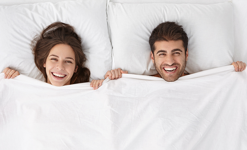 A couple lying in a hotel bed and laughing