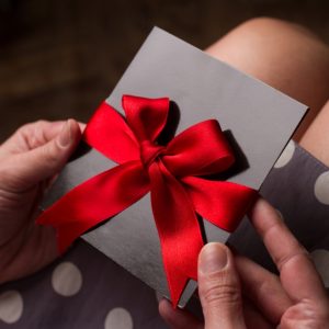 A lady holding a luxurious gift voucher in a black gloss envelope with a bright red bow