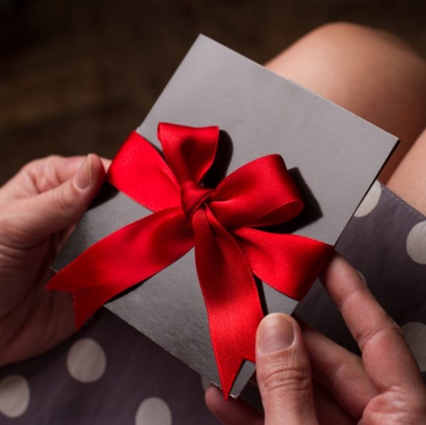 A lady holding a luxurious gift voucher in a black gloss envelope with a bright red bow
