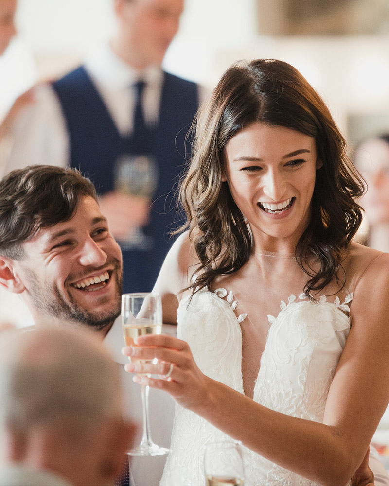 A bride holding up her glass of champagne and laughing