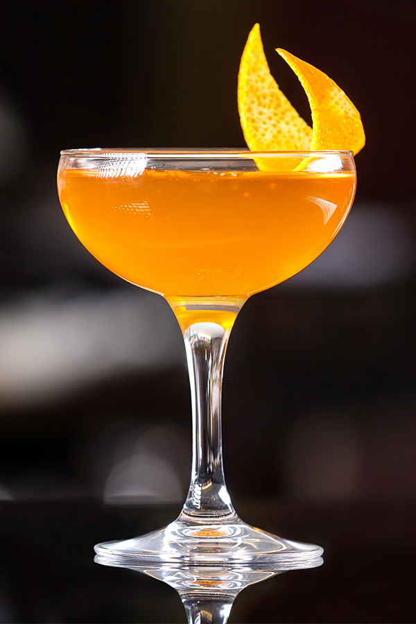 An orange cocktail with a slice of lemon