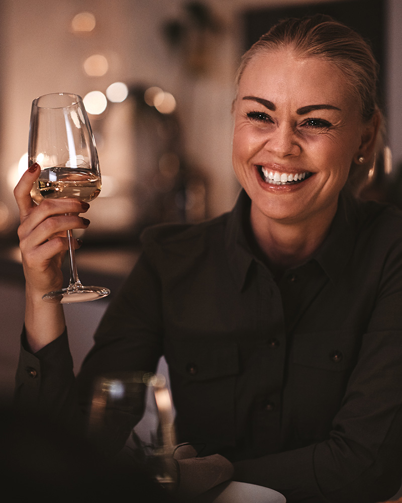 A woman laughing while dining and enjoying a glass of white wine