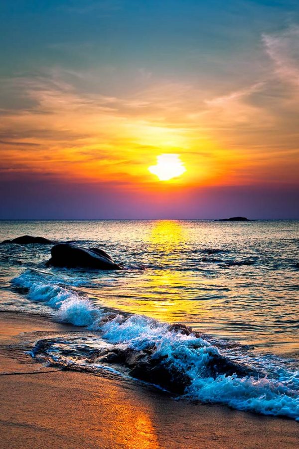 A beach with a setting sun over the waves filling the sky with colour