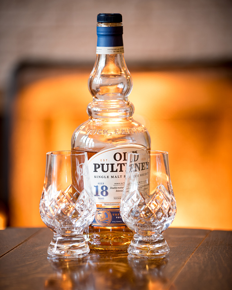 Old Pulteney Whisky and two empty whisky glasses with a roaring fire in the background at Mackays Hotel in Wick