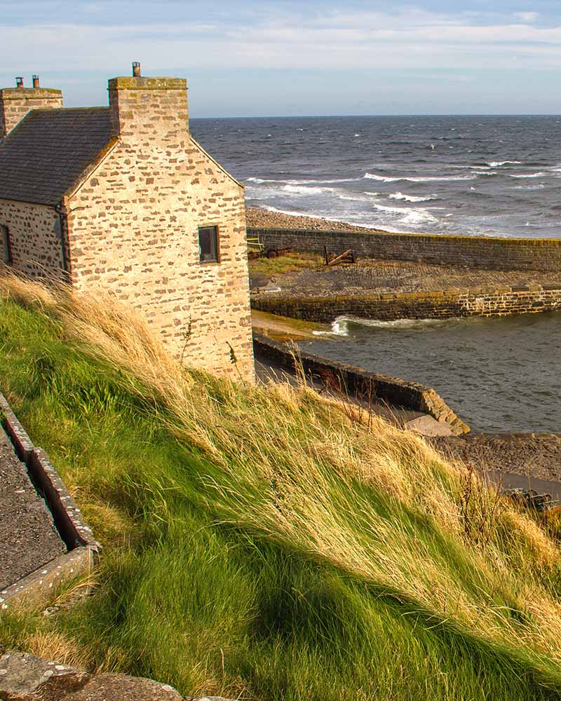 A sea view past an old building and the water way at John O'Groats