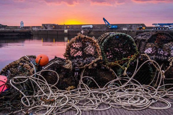 Lobster creels sit on wick harbour with a beautiful sunset sky reflecting on the water