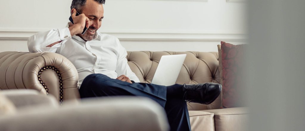 A man working in a hotel lobby as he is on his phone whilst sitting on a sofa.