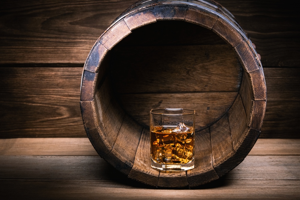 Glass of Scottish whiskey with ice on rustic whiskey barrel on a wooden table