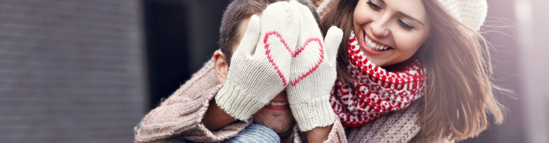 Woman covering her partner's eyes wearing mittens with a heart