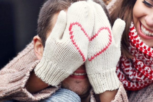 Woman covering her partner's eyes wearing mittens with a heart