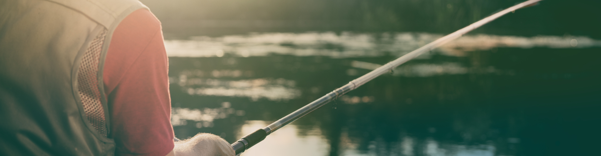 fishing rod close up with a man fishing into a river with the sunrise in front of him.