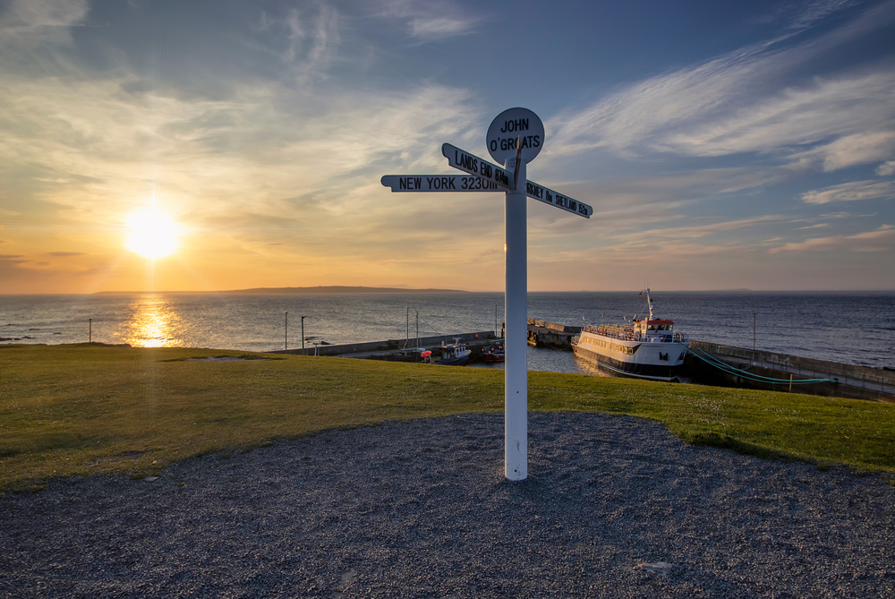 The sun setting behind the iconic signpost at John O'Groats in the Scottish Highlands, UK