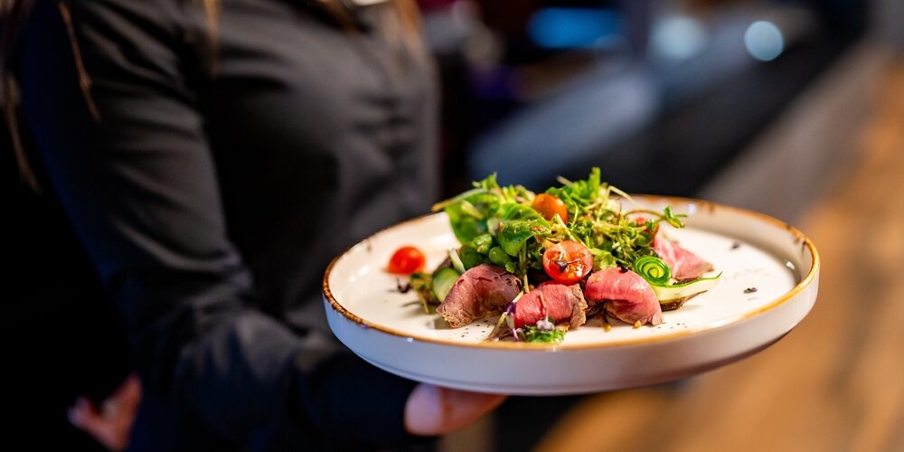 Person holding a plate of gourmet salad with seared tuna. The image captures the art of fine dining and beautifully presented dish.